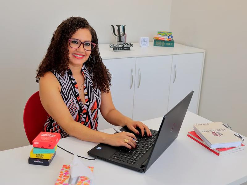 Profissional do NASP em um consultório, sentada à mesa com notebook e materiais de trabalho